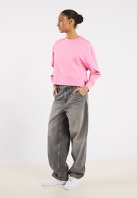 Felpa rosa corta con collo tondo, abbinata a jeans grigi oversize e sneakers bianche, caratterizzata da una vestibilità rilassata e una texture morbida.