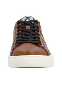 Brown leather sneaker with black laces, textured surface, white rubber sole, and a patterned tongue label featuring a logo.