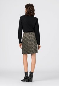 Mustapaita korkealla kaula-aukolla yhdistettynä polven pituisiin kuvioituihin hameisiin vihreän ja ruskean sävyissä, varustettuna mustilla nilkkakoreilla.