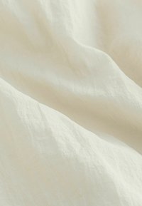 Tissu texturé beige clair drapé en plis doux, présentant une surface légèrement irrégulière avec une finition lisse et des fibres naturelles.