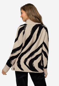 Beige Pullover mit einem schwarzen Zebra-Streifenmuster, geripptem Ausschnitt und Bündchen sowie einer lockeren Passform mit einem etwas längeren Rückensaum.
