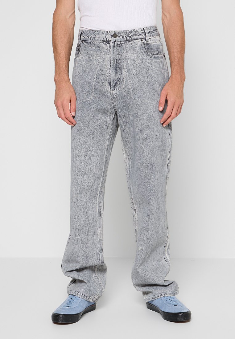 Vooraanzicht van een persoon die lichtgrijze acid-wash jeans, een witte tanktop en lichtblauwe sneakers met zwarte zolen draagt.