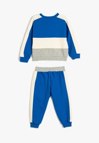 Blå och krämrandig sweatshirt med grå detaljer, som matchas med blå sweatpants. Båda är gjorda av mjukt, texturerat material.