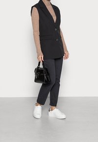 Black sleeveless blazer with two front pockets, paired with a brown ribbed turtleneck, dark jeans, white sneakers, and a black crocodile-textured bag.