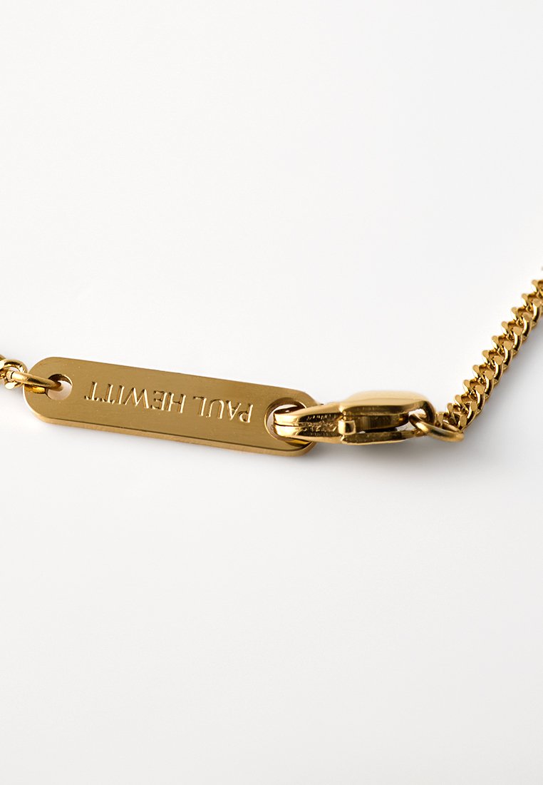 Goldkettchen mit einem flachen Anhänger, der mit "PAUL HEWITT" graviert ist. Es hat einen Karabinerverschluss und Glieder mit einer sanften Textur.