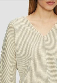 Lichtgekleurde V-hals top met smalle verticale strepen in beige. Zachte, gestructureerde stof met een ontspannen pasvorm en brede mouwen.