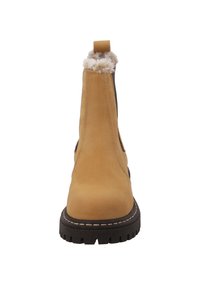 Botte cheville en suede beige avec doublure en fausse fourrure blanche sur le dessus, bout rond et semelle en caoutchouc noir avec des détails de crampons texturés.