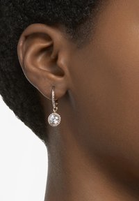 Pendientes de aro en oro rosa con un cristal circular colgante rodeado de cristales más pequeños, que exhiben un acabado texturizado y un diseño elegante.