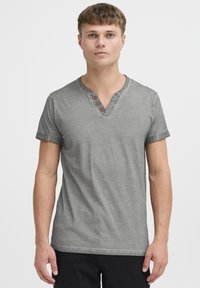 Camiseta gris de manga corta con escote en V y tres botones de madera, con una textura suave y mangas enrolladas, llevada por una persona.
