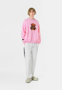 Sudadera rosa con diseño de osito de peluche, combinada con pantalones cargo blancos y zapatos de lona texturizados. Líneas limpias y corte casual.