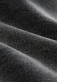 Gros plan d’un tissu noir doux et texturé avec un motif de tissage diagonal visible et des plis doux créant des ombres et des reflets.