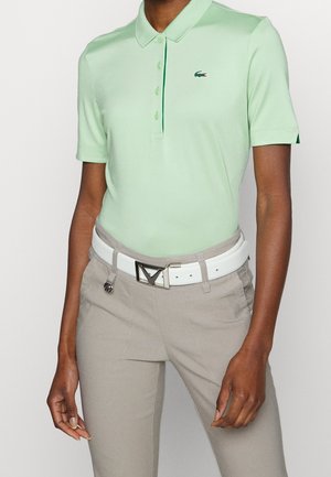 Lichtgroene polo met korte mouwen en klein krokodillenlogo, gecombineerd met beige broek en witte riem met een zilveren gesp.