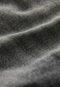 Grijs denim stof met een gladde textuur, voorzien van subtiele ribbels en variaties in schaduw. Details tonen een close-up van de weving.