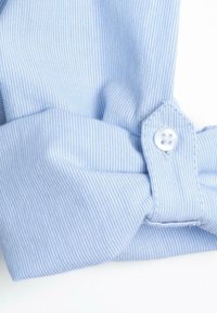 Tessuto a righe blu chiaro con una piega e un dettaglio a bottone sul polsino, caratterizzato da una forma arrotondata e una texture liscia.