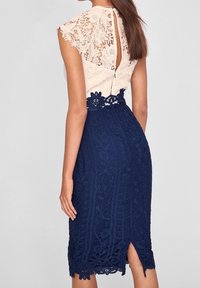 Krajkované šaty s nahým topem a krátkými rukávy, texturovaná sukně v námořnické modré barvě s květinovými vzory a výřezem na zádech ve tvaru klíče.