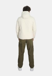 Giacca a vento bianca con cappuccio, tessuto testurizzato e dettagli cuciti, abbinata a pantaloni cargo color oliva e sneakers bianche.