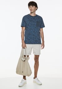 Námořnické modré tričko s vzorem listů, se skládající kapsou na hrudi; doplněné béžovými šortkami a lehkou taškou. Bílé tenisky outfit dokončují.