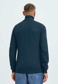 Dunkeltürkis gestrickter Pullover mit hohem Kragen, gerippten Manschetten und Saum. Besitzt eine glatte Textur und eine lockere Passform. Rückansicht gezeigt.