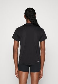 Czarny krótki rękaw sportowej koszulki o gładkiej fakturze, z kontrastowymi przeszyciami i luźnym krojem, widziany od tyłu.