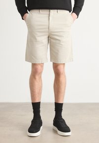 Beige cotton shorts with a straight cut, side pockets, and a smooth texture, paired with black sneakers and crew socks.