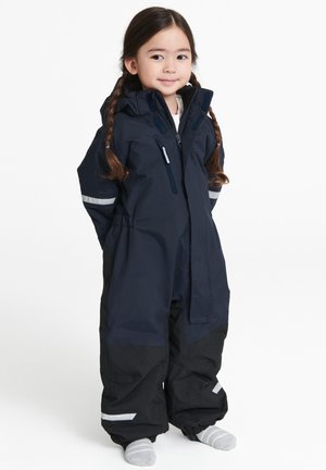 Marine vandtæt jumpsuit med sorte accenter; har en hætte, reflekterende striber og elastiske manchetter. Designet til brug i koldt vejr.