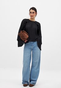 Black ribbed top with ruffled accents, paired with wide-leg light blue jeans. Model holding a brown suede bag, standing on a plain background.