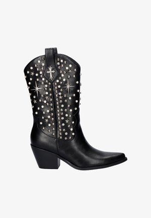 Botas de vaquero de cuero negro con punta afilada, adornadas con tachuelas y estrellas plateadas, y un tacón bajo en forma de bloque. Presentan un detalle en forma de cruz.