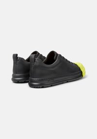 Schwarze Ledersneaker mit einer runden, leuchtend gelben Gummispitze, die ein niedriges Profil und strukturierte Seitenpaneele aufweisen.