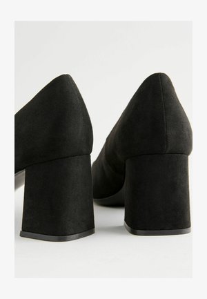 Czarne zamszowe buty na wysokim obcasie z szerokim obcasem. Posiadają szpiczasty czubek i gładką fakturę, prezentując minimalistyczny design.