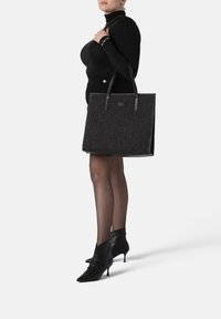 Zwarte tote bag gemaakt van textuurstof met leren accenten, met twee stevige handvatten en een gestructureerde vorm.