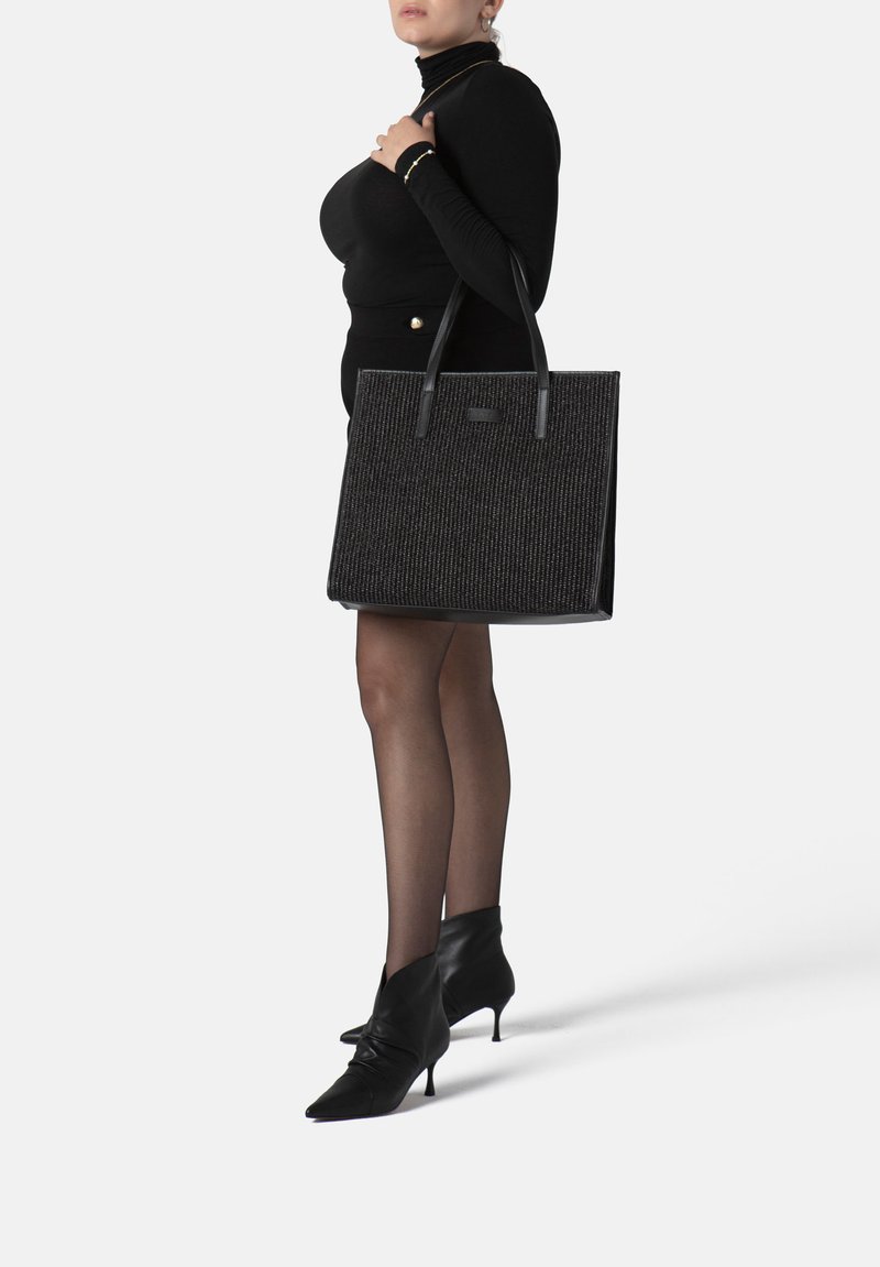 Zwarte tote bag gemaakt van textuurstof met leren accenten, met twee stevige handvatten en een gestructureerde vorm.