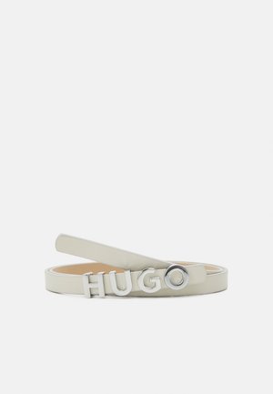 Lys beige læderbælte med sølvmetalbogstaver, der staver "HUGO" som spændet, vist fladt på en hvid baggrund.