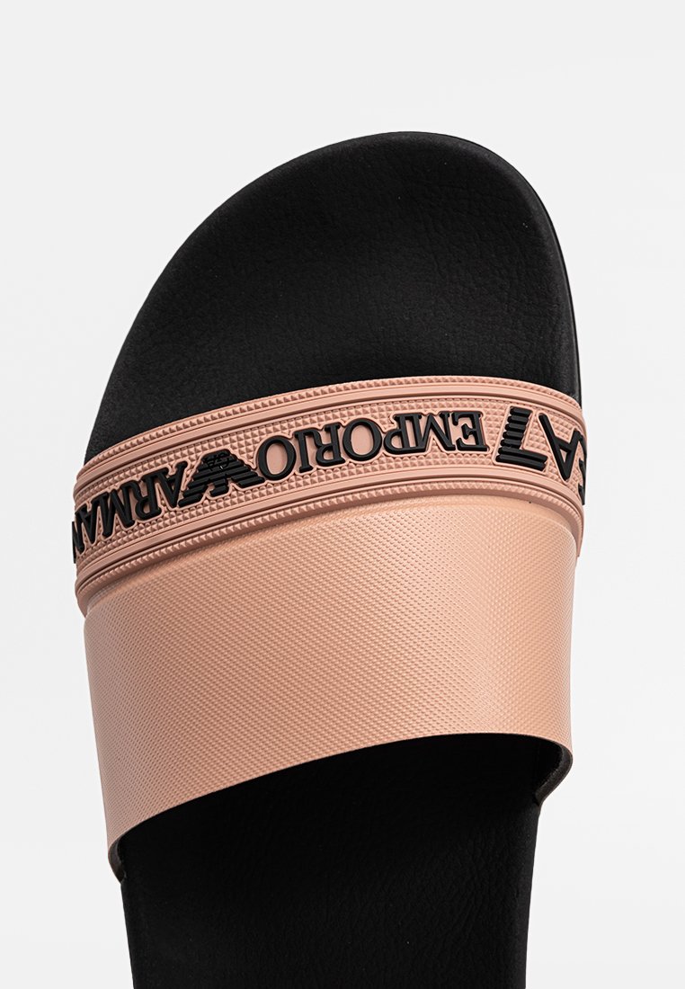 Chancla negra con una tira texturizada rosa que presenta letras y un logotipo en negro. Material interior suave con un diseño de color contrastante.