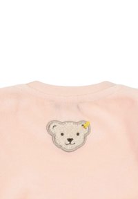 Prenda de color rosa claro que presenta un parche con la cara de un oso texturizado y un detalle amarillo, situado en la parte posterior del cuello. Tejido suave y cuello redondo.