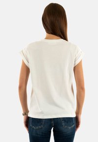 Camiseta blanca de algodón con mangas cortas enrolladas, cuello redondo y un corte holgado. Combinada con unos vaqueros de mezclilla azul oscuro. Diseño sencillo y casual.