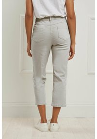 Pantalones gris cortos con un ajuste entallado, bolsillos delanteros y traseros, y una cintura alta. Combinados con zapatillas blancas sobre un suelo de madera clara.