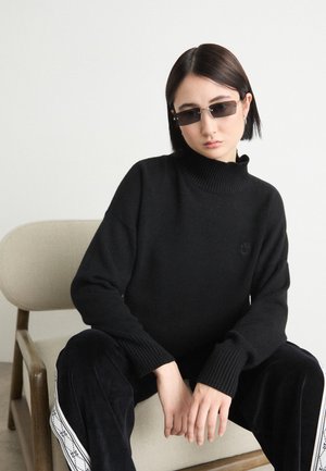 Black knitted sweater with a high collar and ribbed cuffs, paired with dark pants featuring side stripes. Smooth texture and minimal design details.