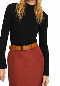 Schwarzes geripptes Langarmoberteil kombiniert mit einem rostfarbenen Rock. Brauner Leder-Gürtel mit metallic Schnalle. Strukturiertes Gewebe sichtbar.