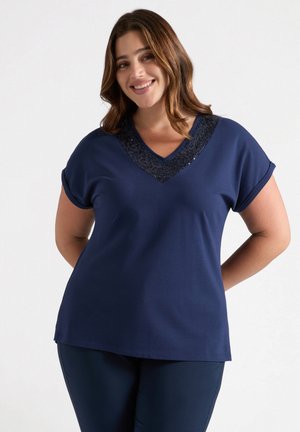 Top de manga corta en azul marino con escote en V y cuello adornado con lentejuelas, confeccionado en una tela suave, con un corte relajado y un dobladillo ligeramente curvado.