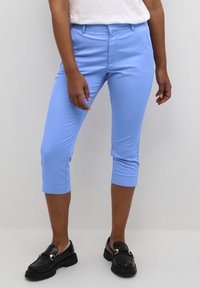 Pantaloni blu chiaro a vita alta realizzati in tessuto elasticizzato, con una texture liscia e un design aderente, abbinati a mocassini neri.