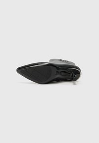 Chaussure à talon haut noire avec un bout pointu, un dessus texturé, une semelle lisse et un accent décoratif. Semelle en caoutchouc avec un motif antidérapant.
