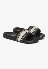 Sandalias de slide negras con tiras de tejido ancho que presentan acentos blancos y estampados, y suelas de goma negra texturizada para mayor agarre.