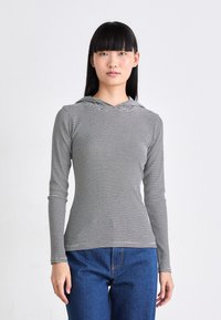 Svarte og hvite stripete langermede topper med hette, laget av lett stoff, figursydd design, kombinert med blå denimjeans.