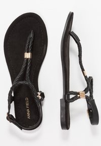 Black flat sandals with braided straps and gold accents, ankle buckle, and "Anna Field" branding on the insole.