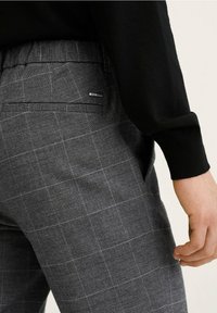 Grijze geruite broek met een gladde textuur, een achterzak en een logo-label. De tailleband is geëlastiseerd voor comfort.