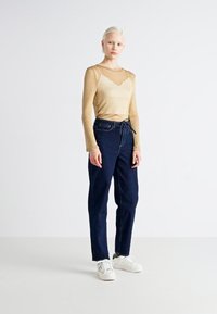 Light beige long-sleeve top with a wavy neckline, paired with dark blue high-waisted pants, complemented by white sneakers.