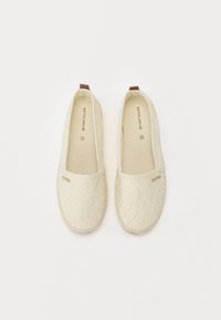 Valkoiset kankaiset slip-on-kengät, joissa on pitsikuvio ja ruskeat korostukset. Litteät pohjat ja pyöreä kärki. Brändin etiketti näkyvissä sisällä.