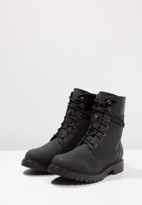 Svarta ankelstövlar med matt finish, med snörning framtill, metalldetaljer och en slitstark sula. Slät textur med glänsande detaljer.