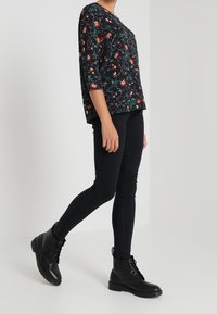 Blusa nera a fiori con maniche a tre quarti, abbinata a jeans skinny neri e stivaletti neri con lacci. Design minimalista e casual.