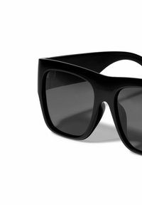 Black oversized sunglasses with a thick frame, angular design, and dark tinted lenses. Smooth texture with minimal detailing.